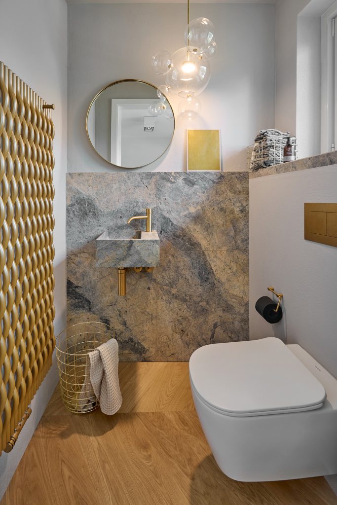 Waschbecken aus Naturstein mit goldenen Armaturen, goldener Heizkörper und Blasenpendelleuchte