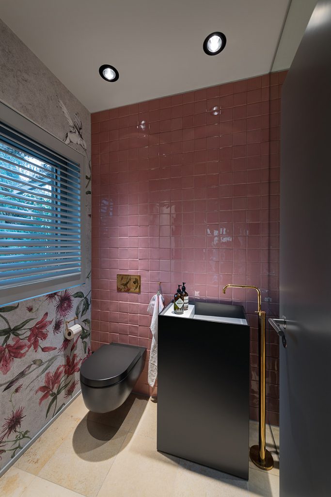 Gäste-WC mit altrosa Fliesen, Blumentapete, schwarzem WC und goldener Standarmatur